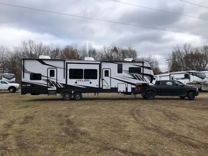 A Valor fifth-wheel toy hauler hitched to a pickup in a grass lot