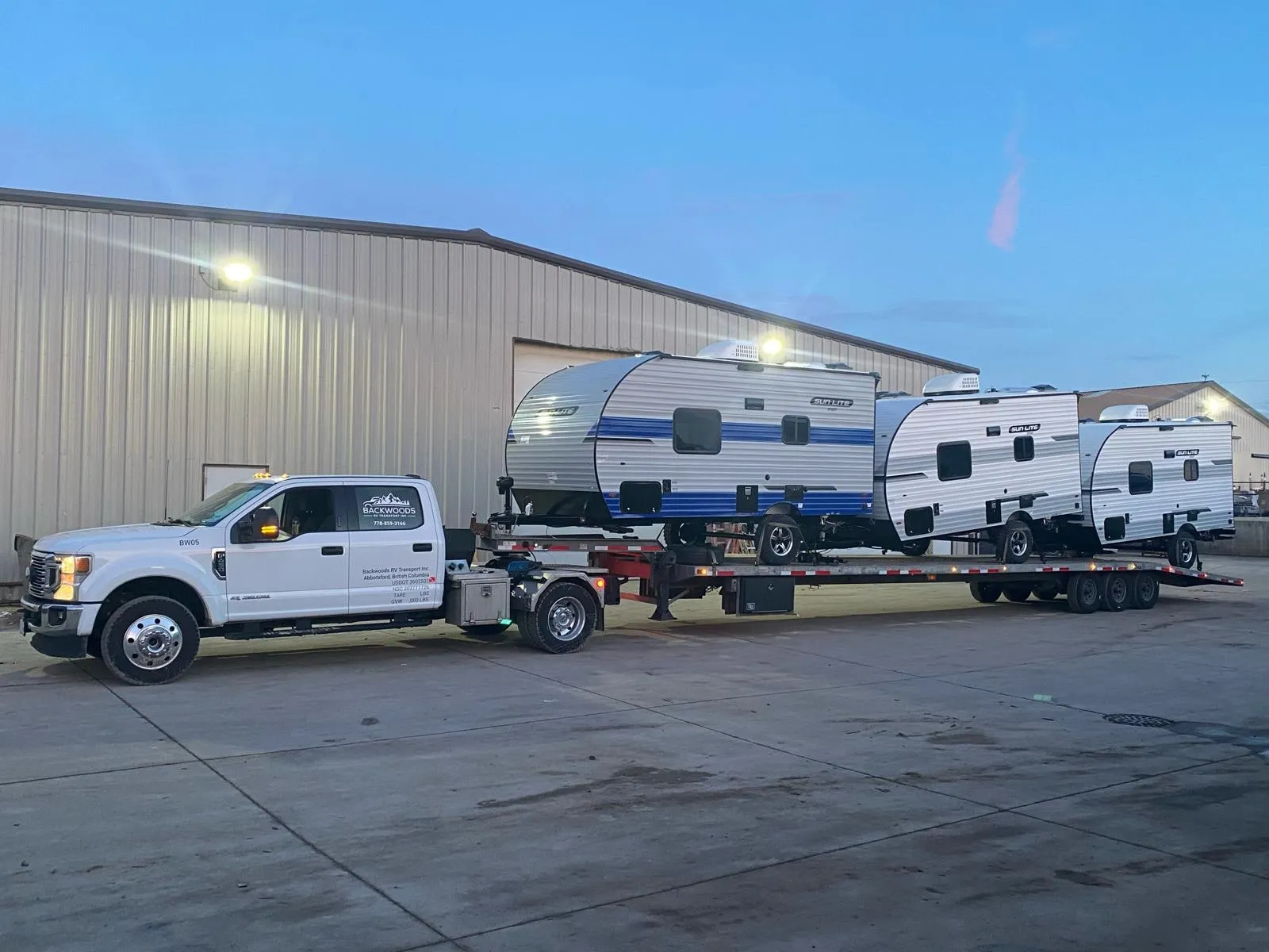 Backwoods pickup with three travel trailers loaded on its deck at dusk